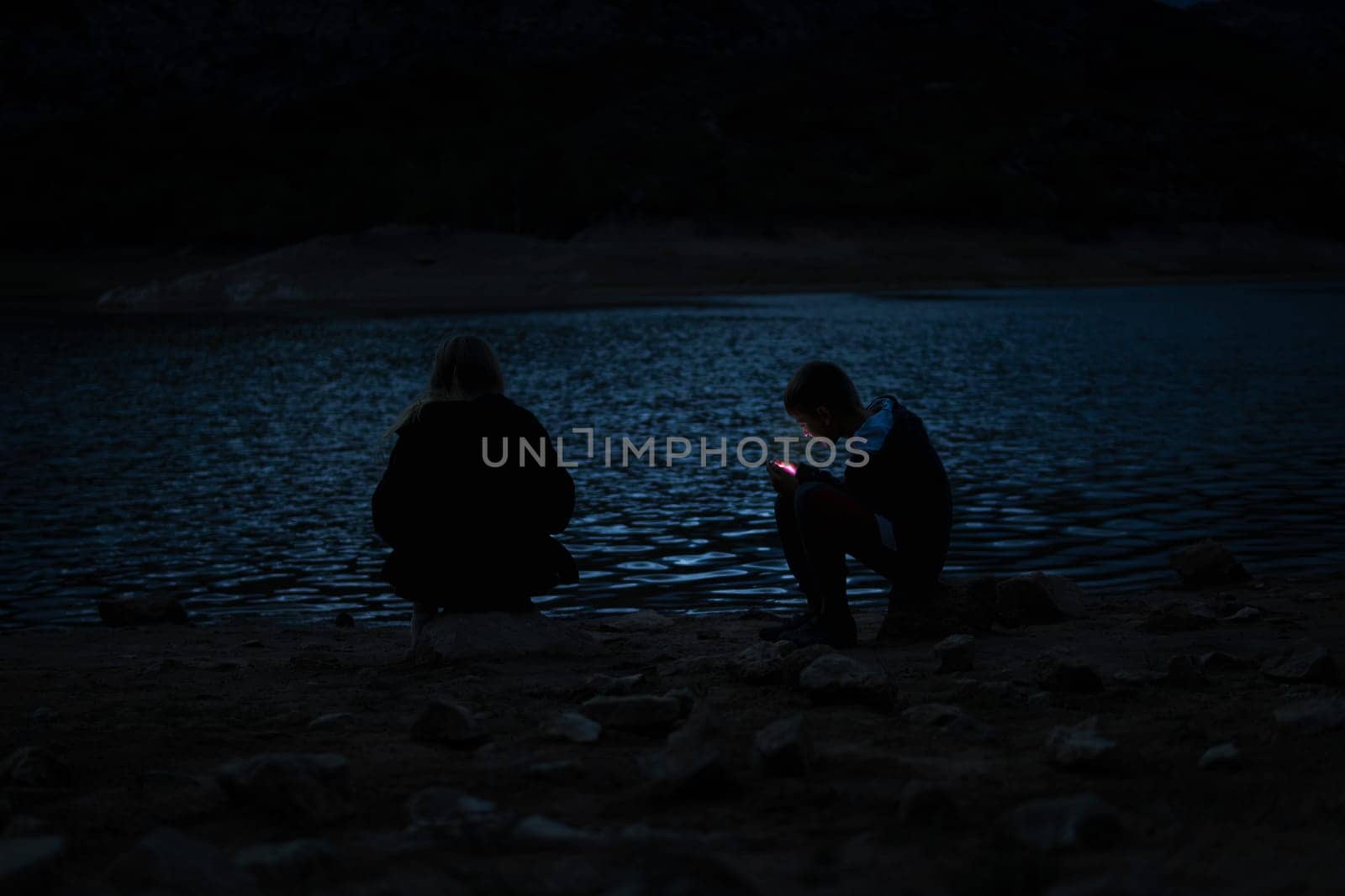 boy and girl sitting near the lake at the campsite in the evening, family vacation concept by PopOff