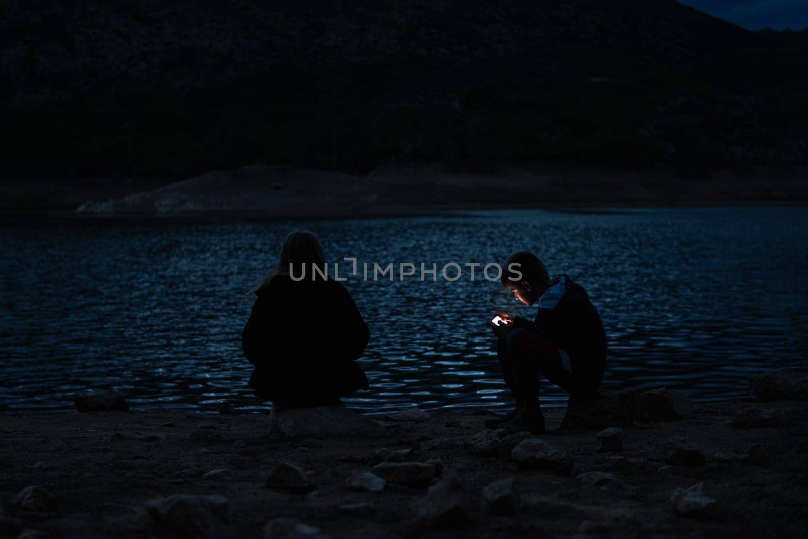 boy and girl sitting near the lake at the campsite in the evening, family vacation concept by PopOff