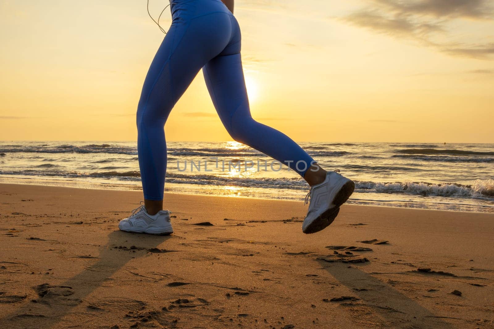 legs of a girl in leggings and sneakers running along the beach at dawn with space for inscription. High quality photo