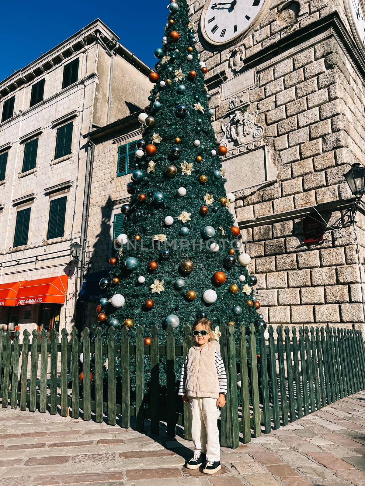 Little girl posing near the Christmas tree near the ancient building. High quality photo