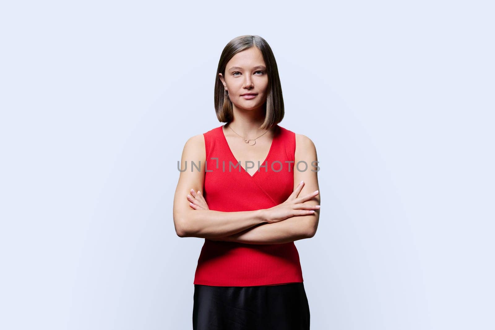 Portrait of young confident woman in red on white studio background. Successful fashionable female with crossed arms looking at camera. Business, work, services, education, fashion beauty professions
