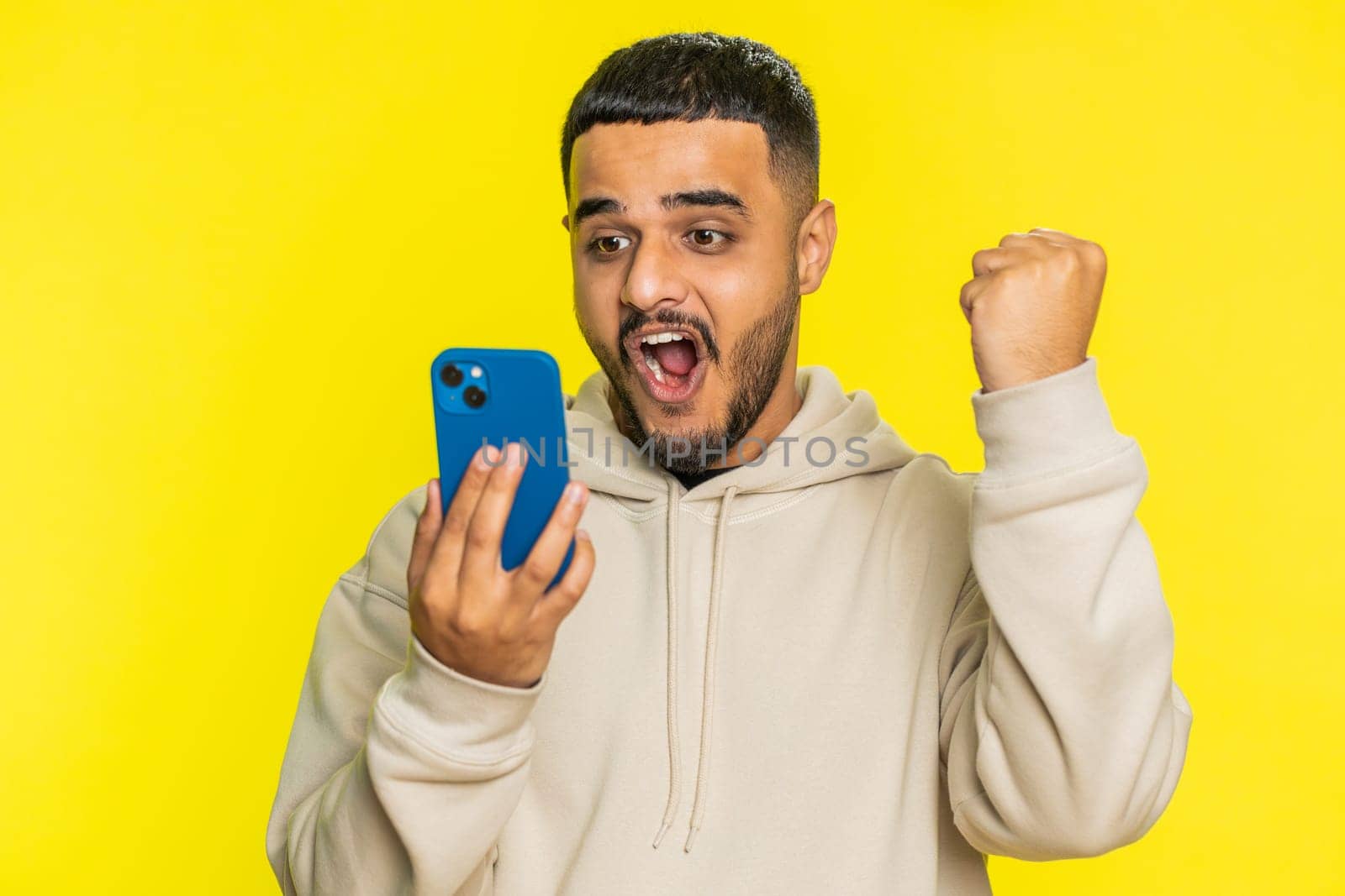 Happy excited Indian Hindu man guy use smartphone typing browsing shouting say wow yes found out great big win good news lottery goal achievement celebrating success, winning play game on yellow
