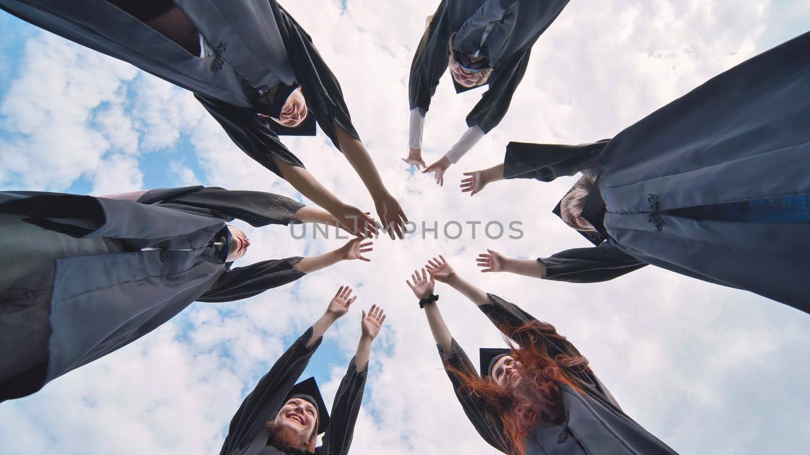 Team of college or university students celebrating graduation. Group of happy successful graduates in academic hats and robes standing in circle and putting their hands together