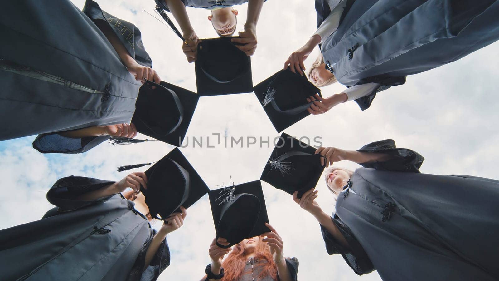 Graduates in black robes join their caps in a circle