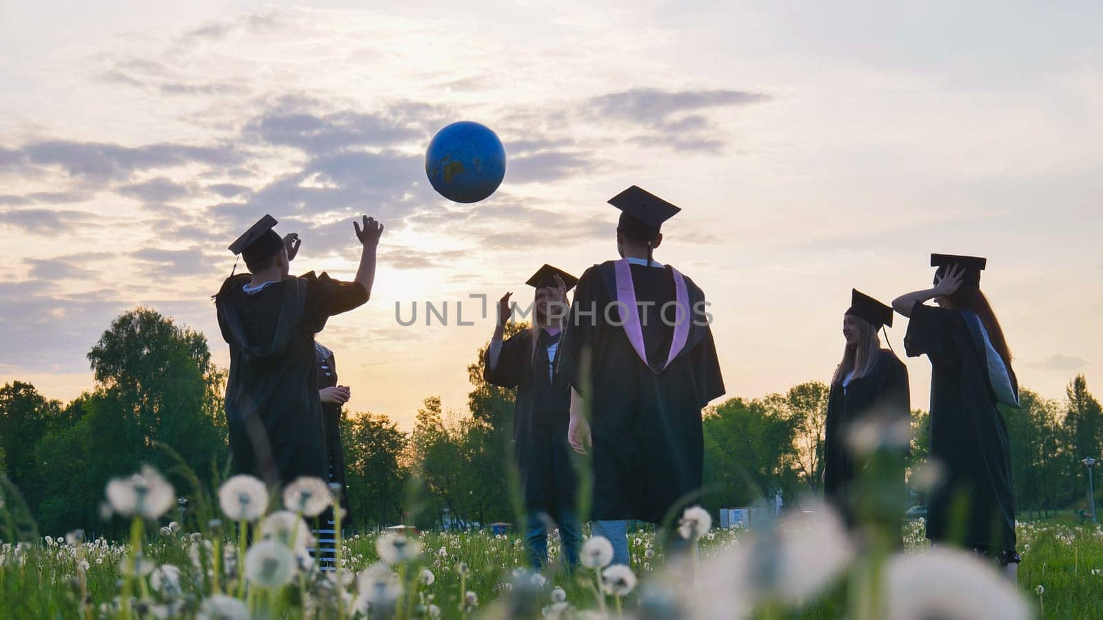 Graduates in costume playing with a ball at sunset. by DovidPro