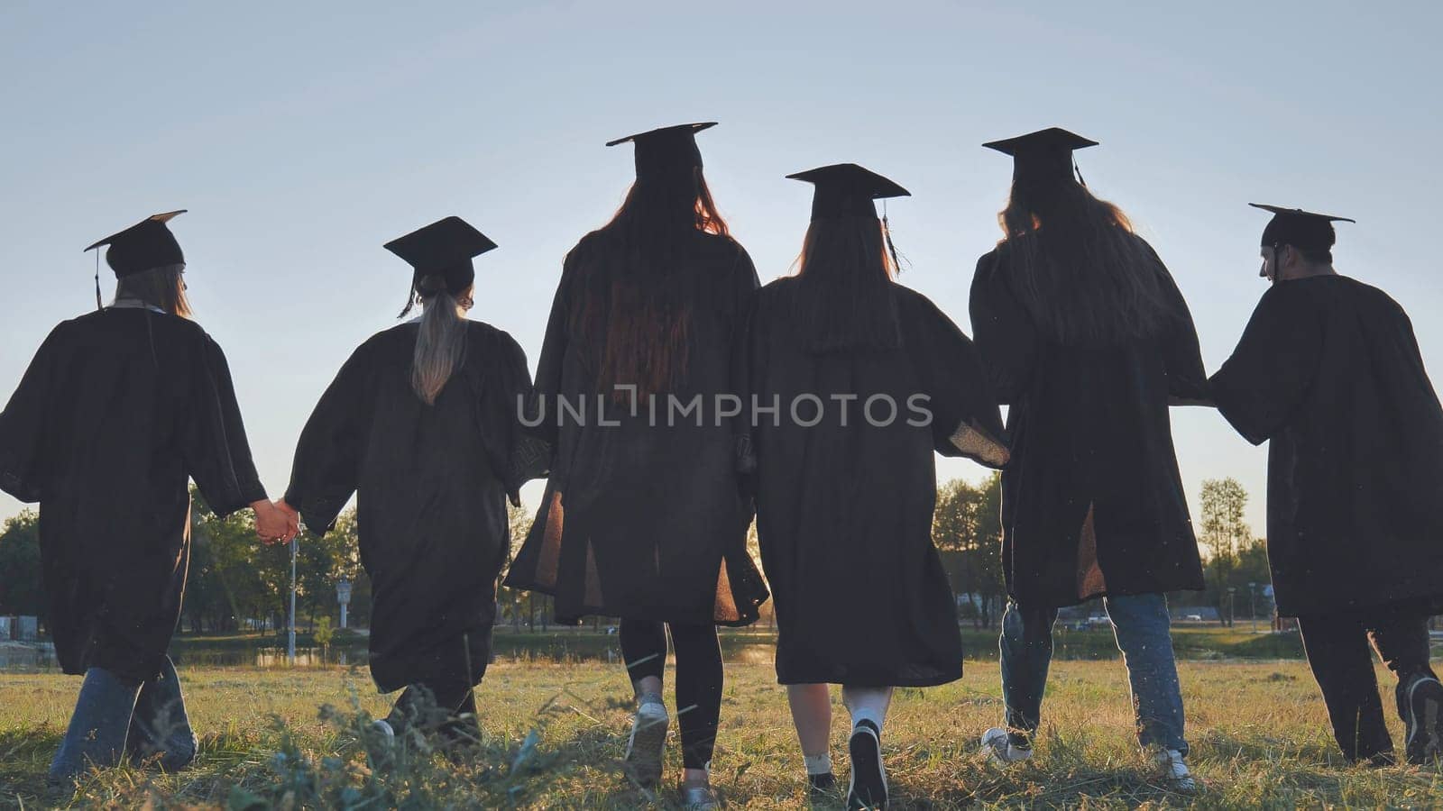 Graduate students walking through an evening meadow at sunset. by DovidPro