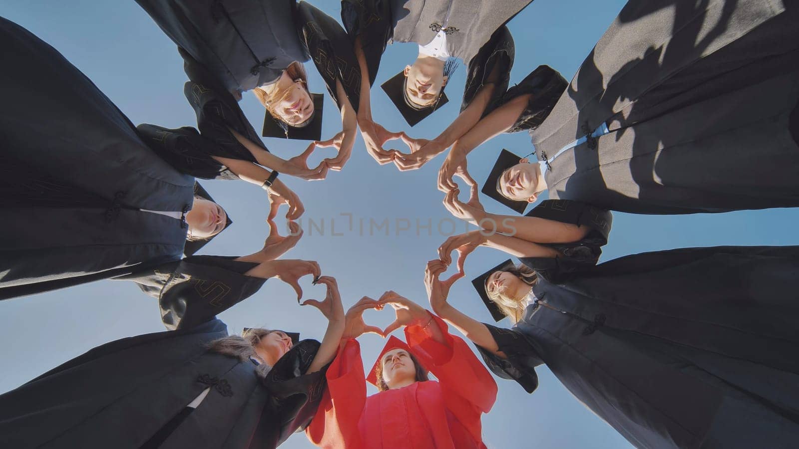 A group of seven college graduates make a heart shape from their hands while standing in a circle wearing robes. by DovidPro
