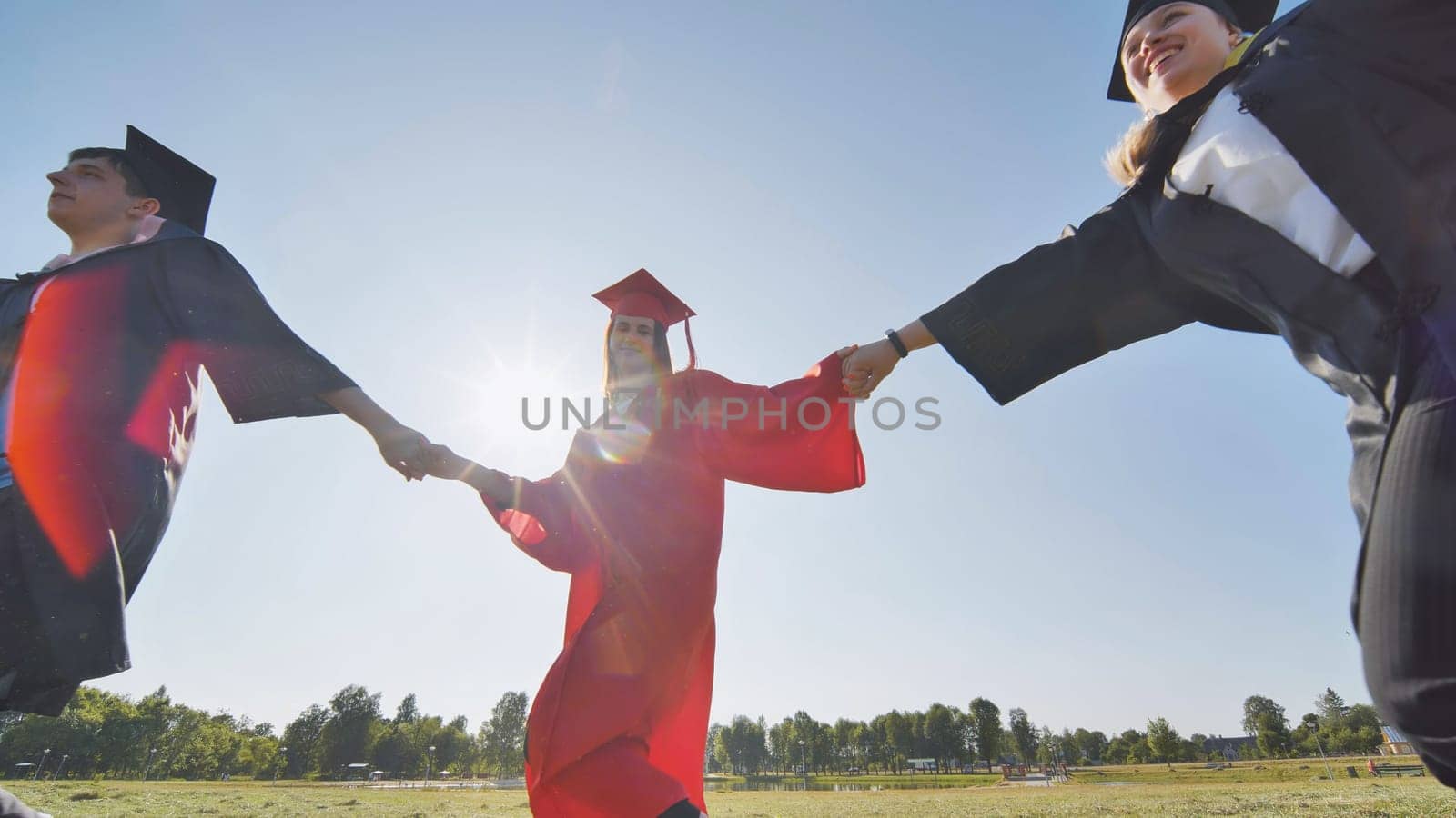 College graduates holding hands run in a round dance. by DovidPro