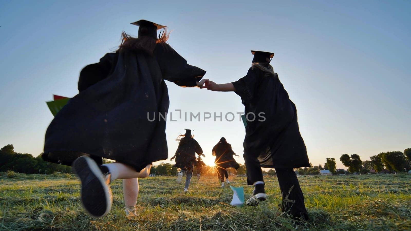 Cheerful graduates students run after school at sunset