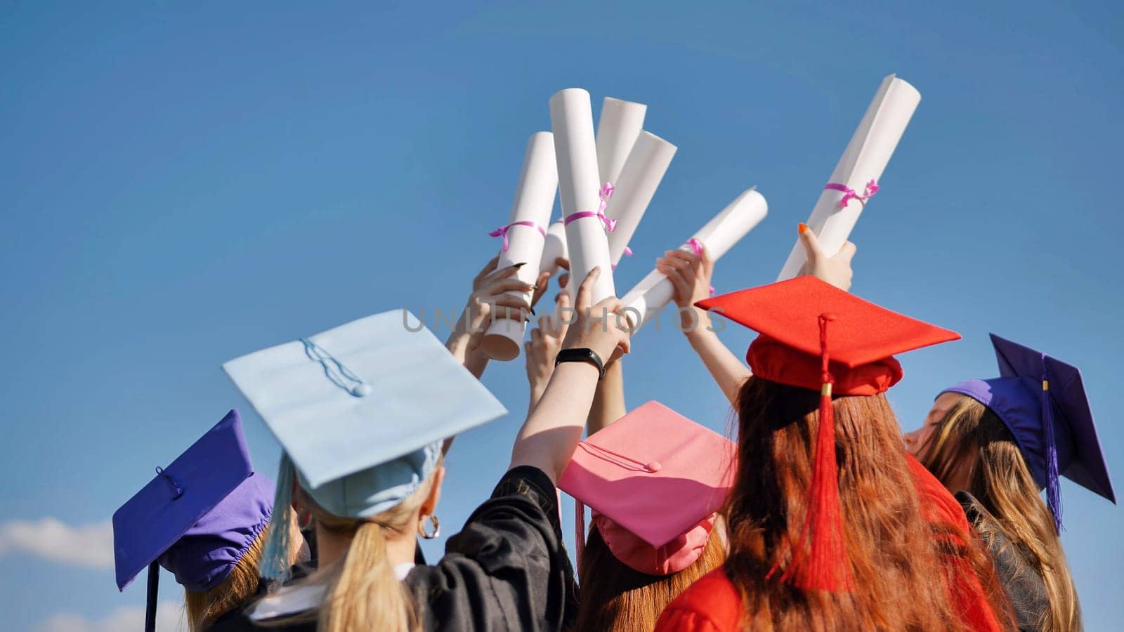 College graduates with caps tie their diplomas together