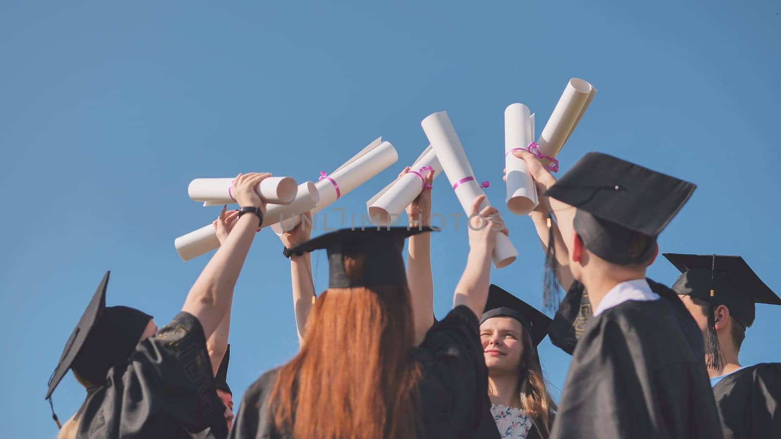 College graduates with caps tie their diplomas together