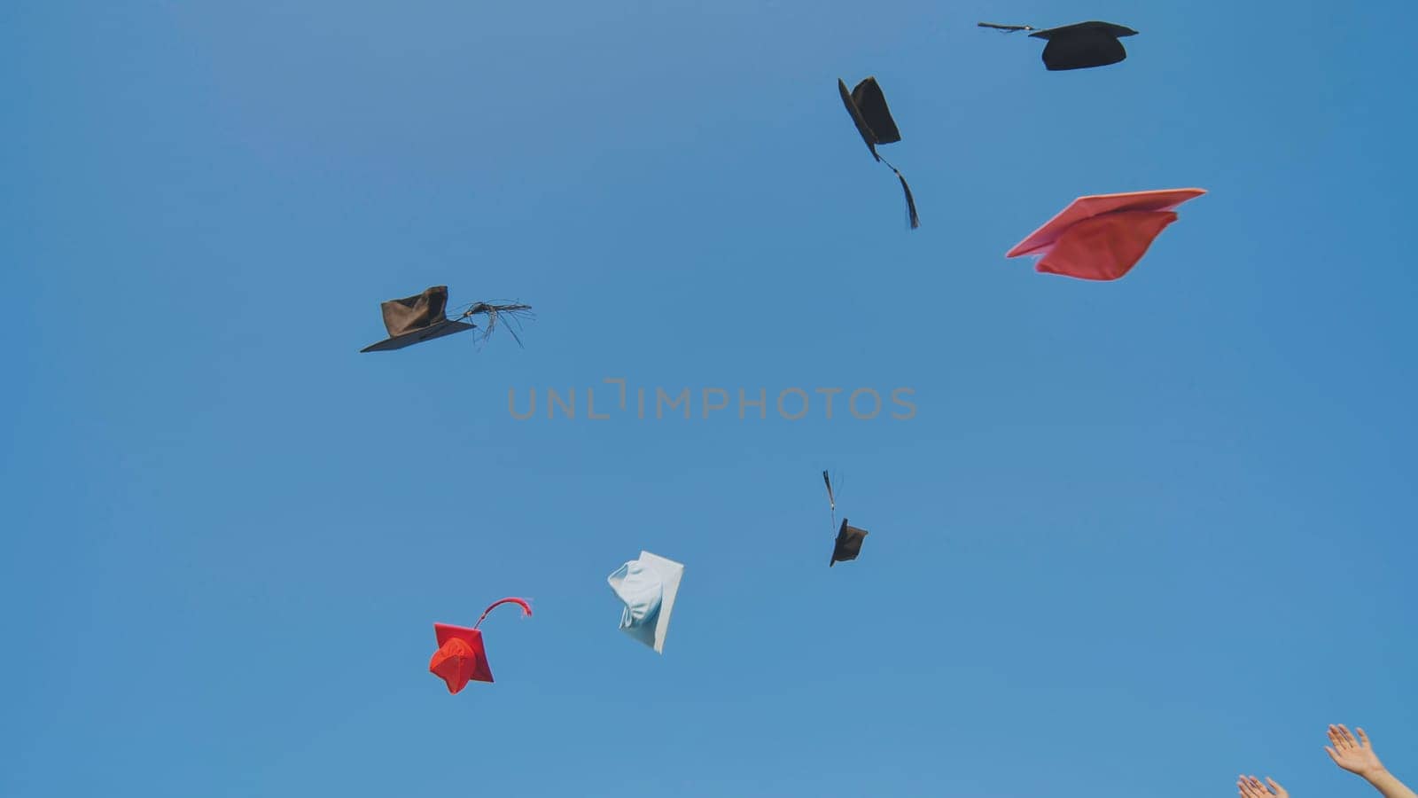 Graduates tossing multicolored hats against a blue sky