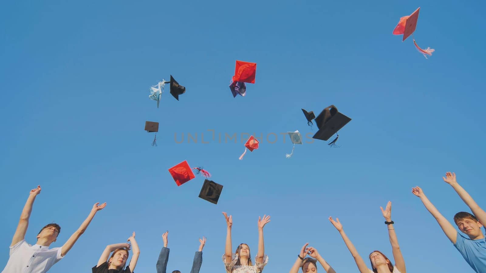 Graduates tossing multicolored hats against a blue sky