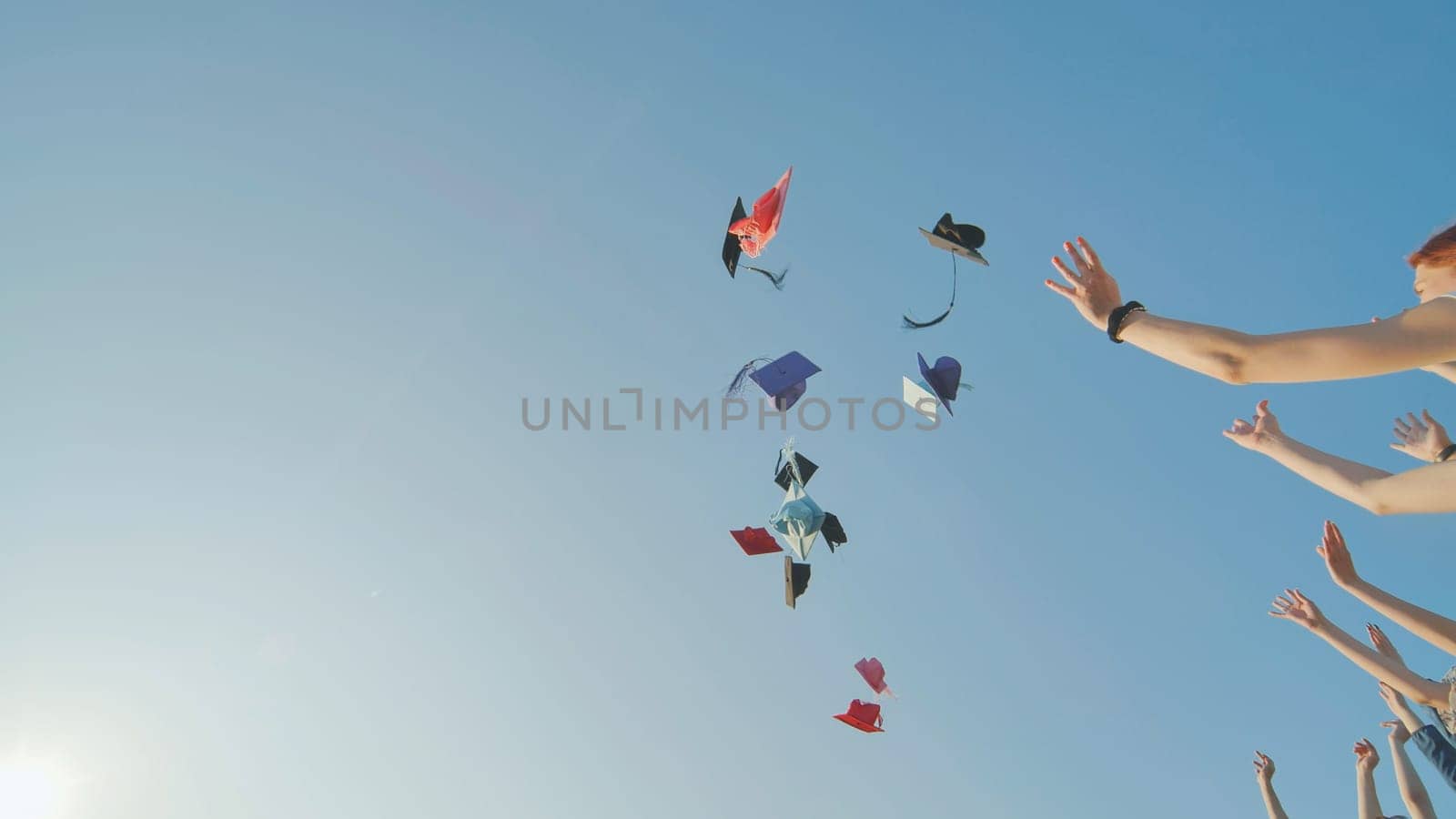 Graduates tossing multicolored hats against a blue sky