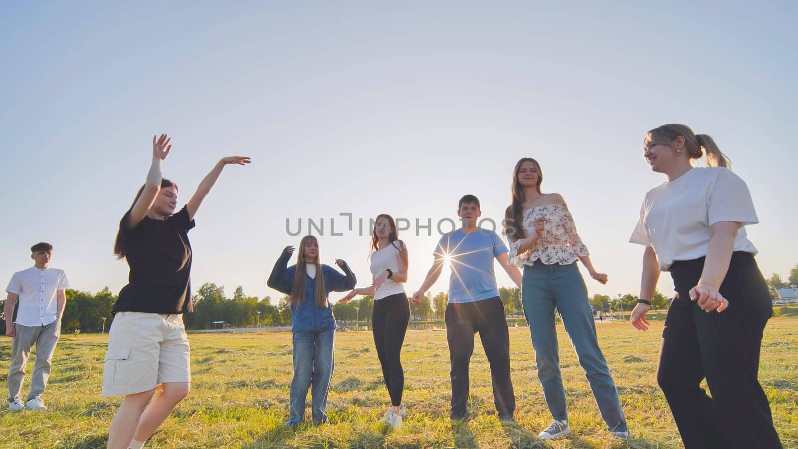 Funny jolly friends dancing in the city meadow in the evening