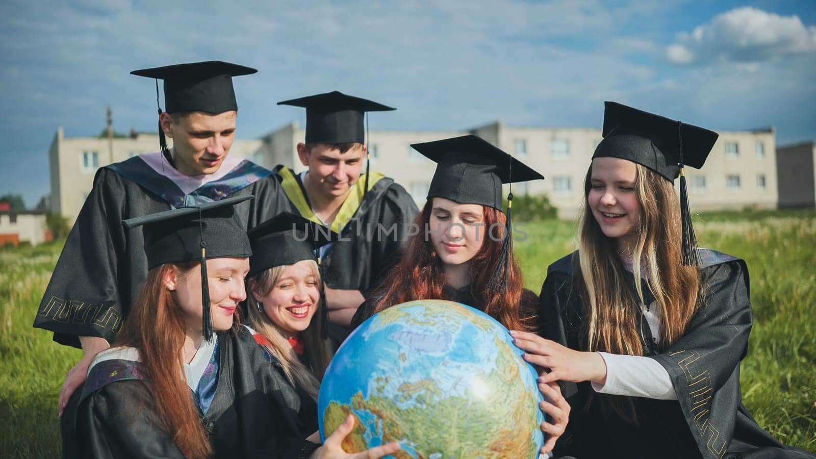 Graduates in black robes examine a geographical globe sitting on the grass