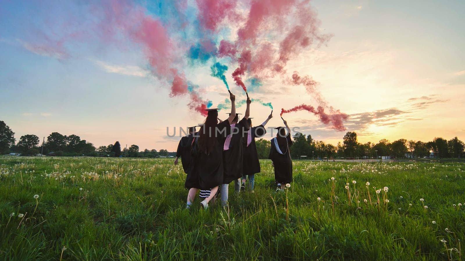 Students graduate with colored smoke walking through the meadow in the evening. by DovidPro