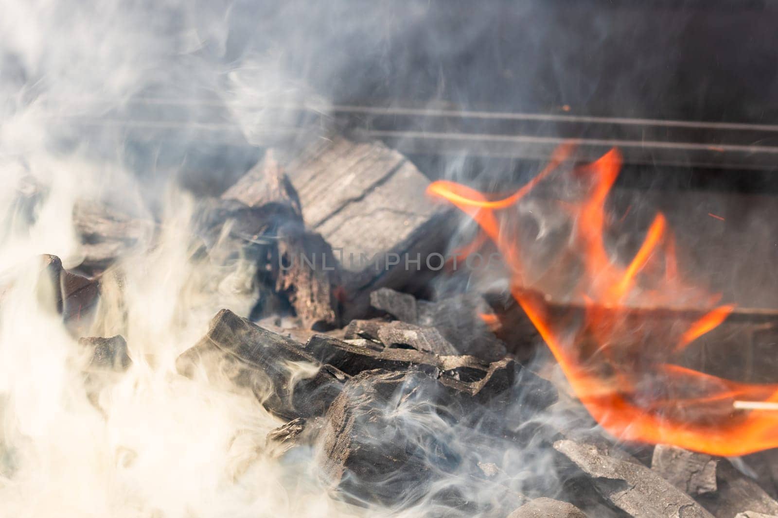 Barbecue grill pit with glowing and flaming hot open fire with red flame, hot charcoal briquettes and embers