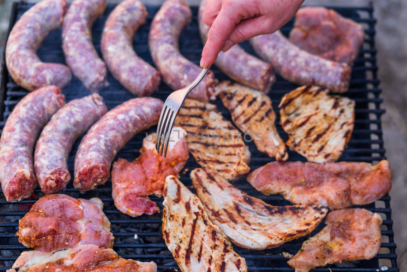 Raw meat on a grill. Sausages and pork meat grilled on a charcoal grill with smoke