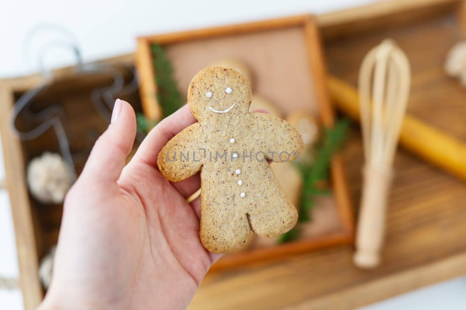 A woman's hand holds a gingerbread man. Cooking gingerbread at home lies on a wooden tray. Holiday concept