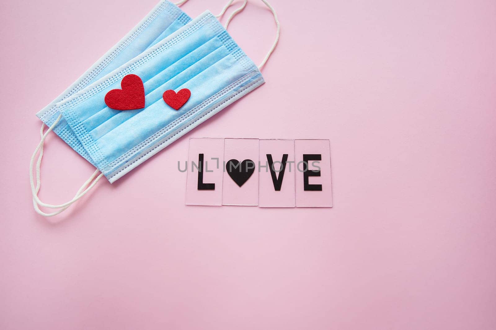 Disposable medical mask and two hearts. Having a baby during the coronavirus pandemic. The inscription love on a pink background