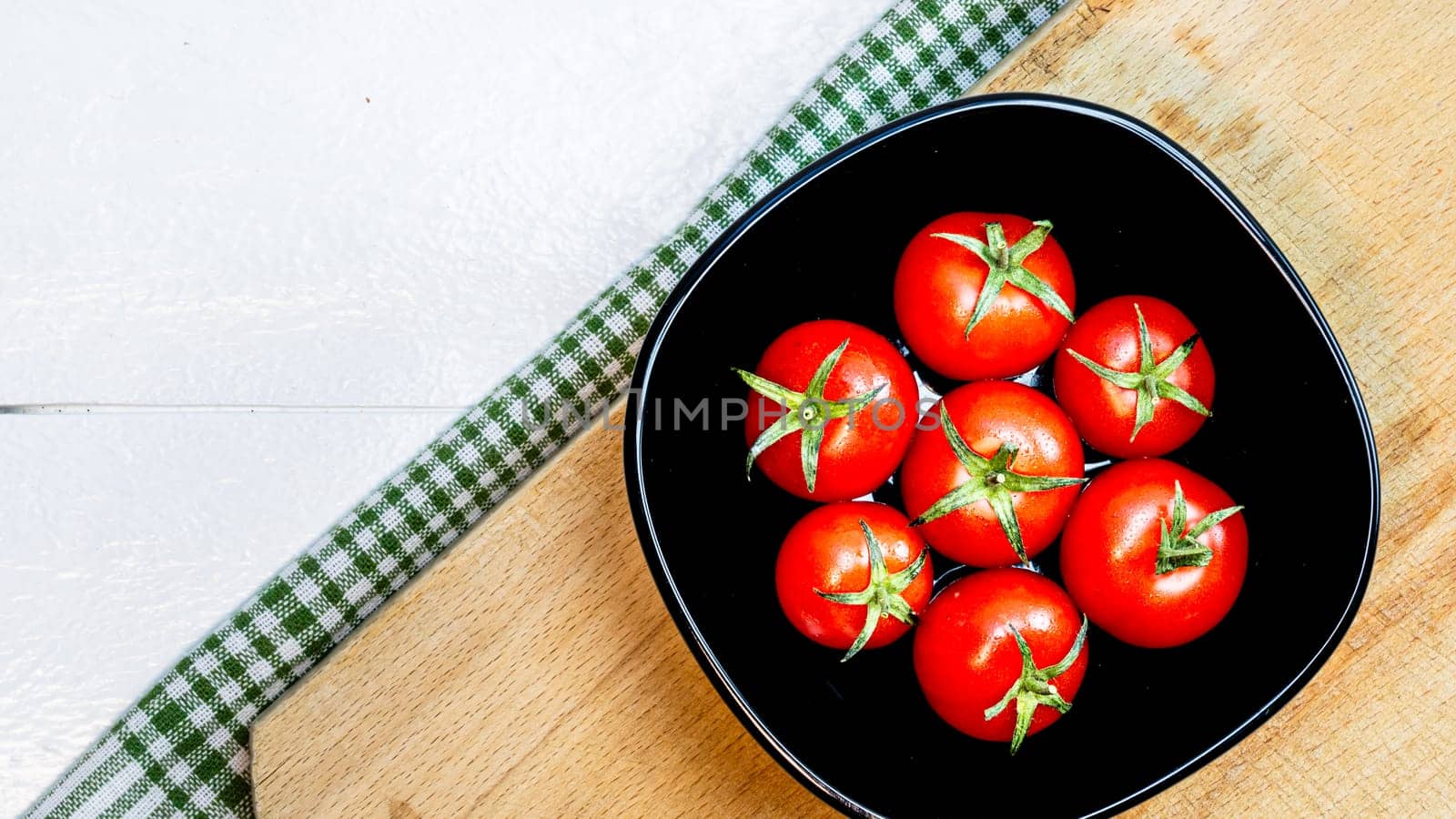 Top view of fresh ripe cherry tomatoes in small black bowl on a rustic white wooden table. Ingredients and food concept