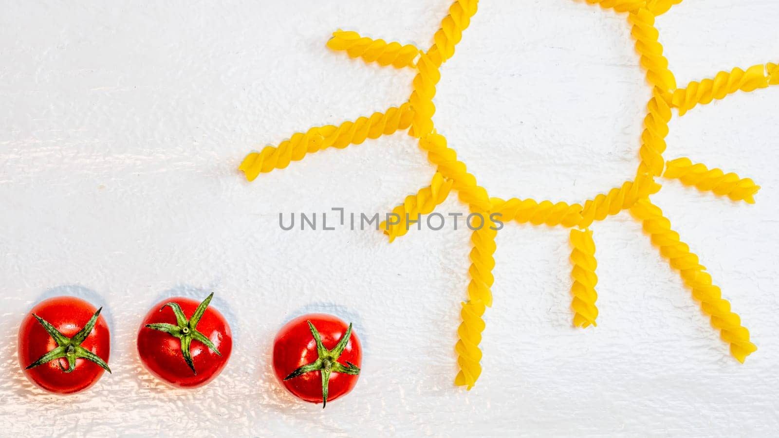 Sun made from fusilli pasta, green field made from green spiral pasta and cherry tomatoes, concept of growing of tomatoes on white background