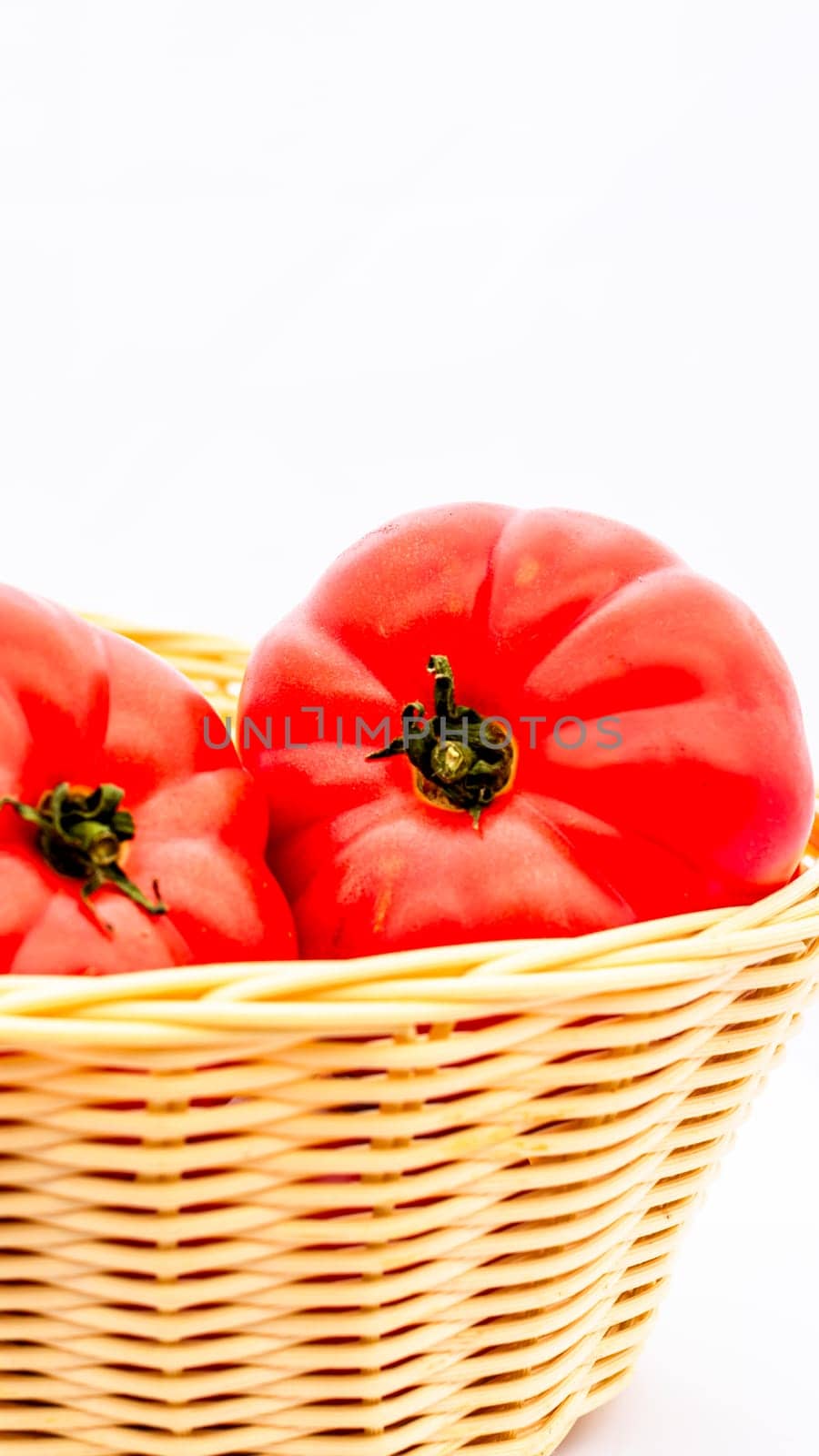 Fresh and tasty red tomatoes in wicker basket isolated