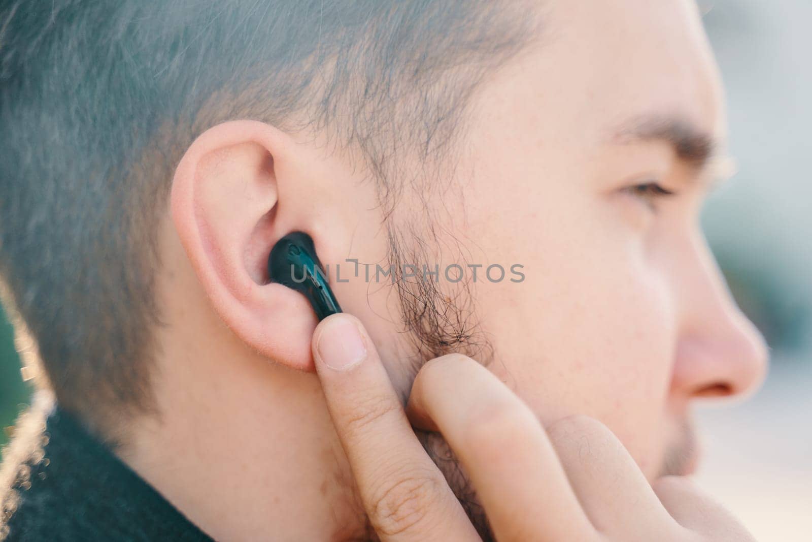 Bishkek, Kyrgyzstan - October 10, 2019: Young man in a coat and wireless custom headphones black apple airpods calls siri and sits in the Park on a bench