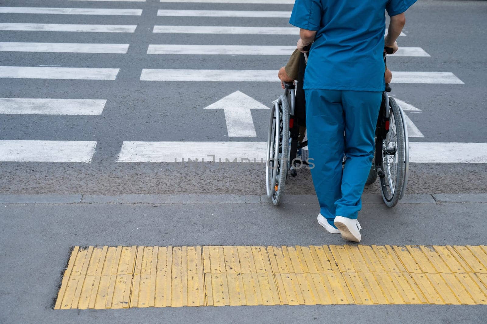 Rear view of a nurse helping an elderly woman in a wheelchair cross the road