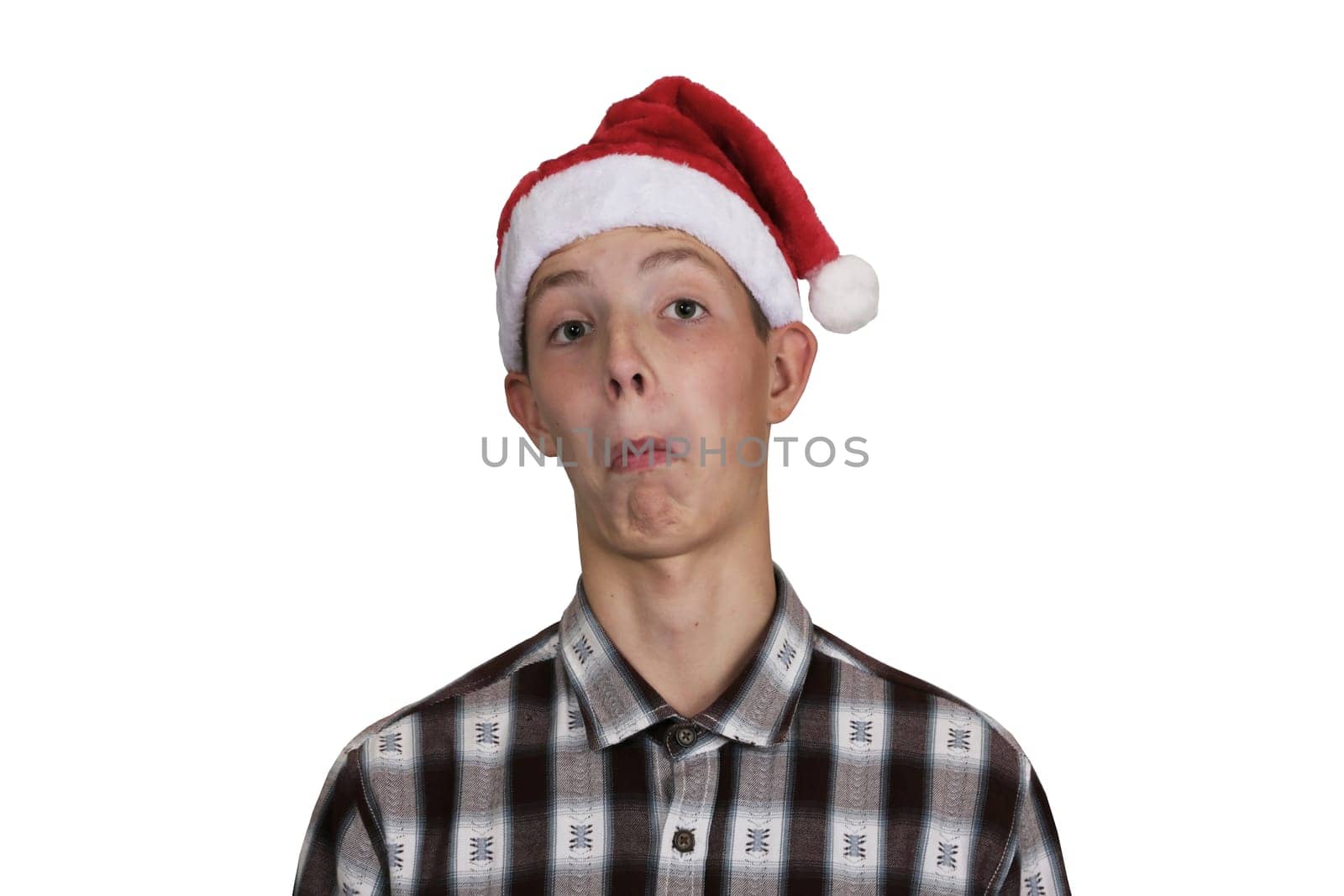Funny, surprised teenage boy in a shirt, wearing a Santa Claus hat, on a white isolated background. The boy makes a grimace.
