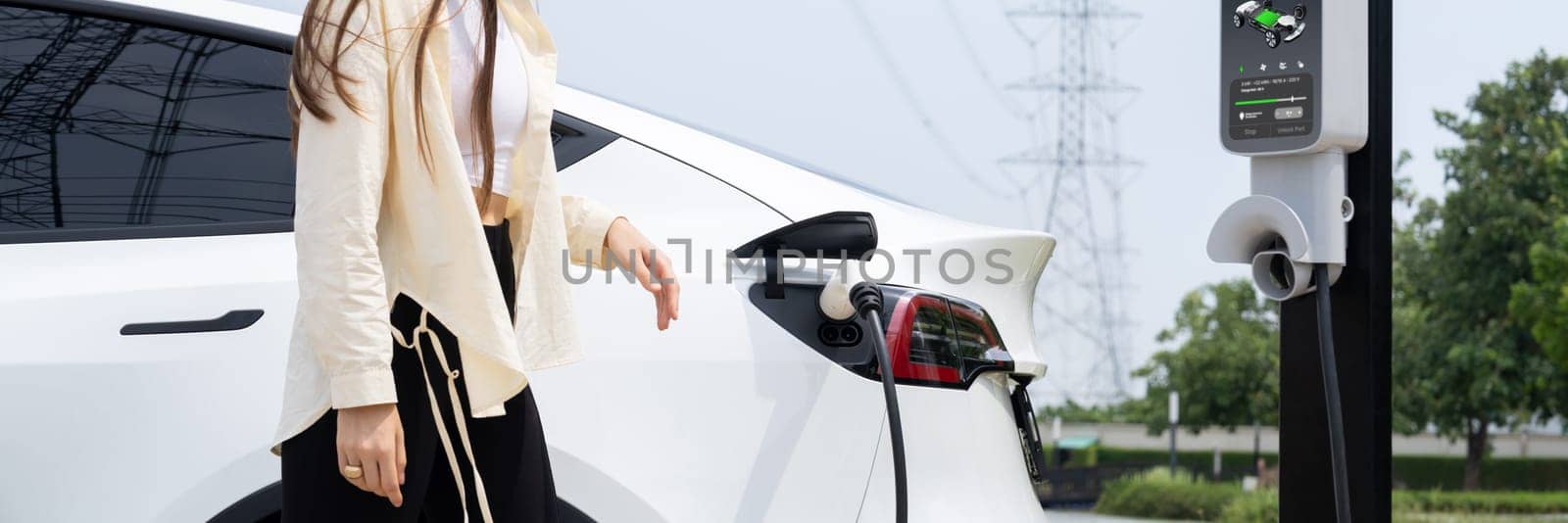 Young woman recharge EV car battery at charging station. Expedient by biancoblue