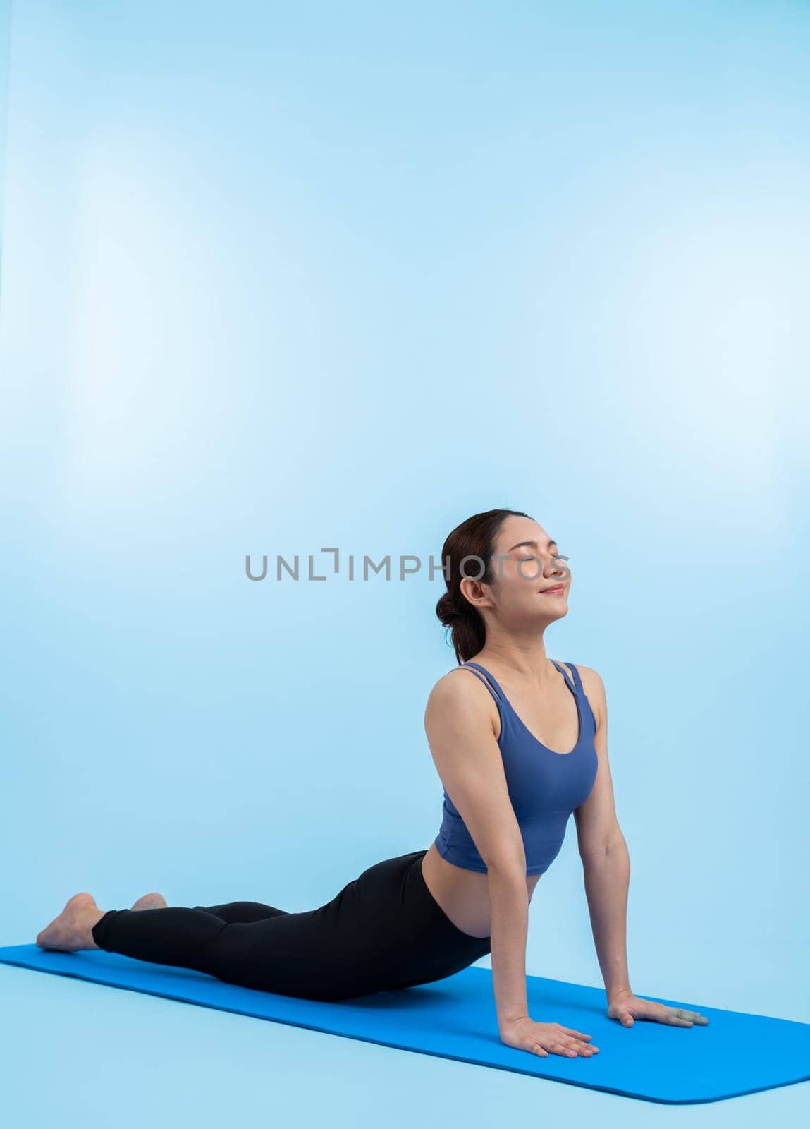 Asian woman in sportswear doing yoga exercise on fitness mat as her workout training routine. Healthy body care and calm meditation in yoga lifestyle in full body shot on isolated background. Vigorous