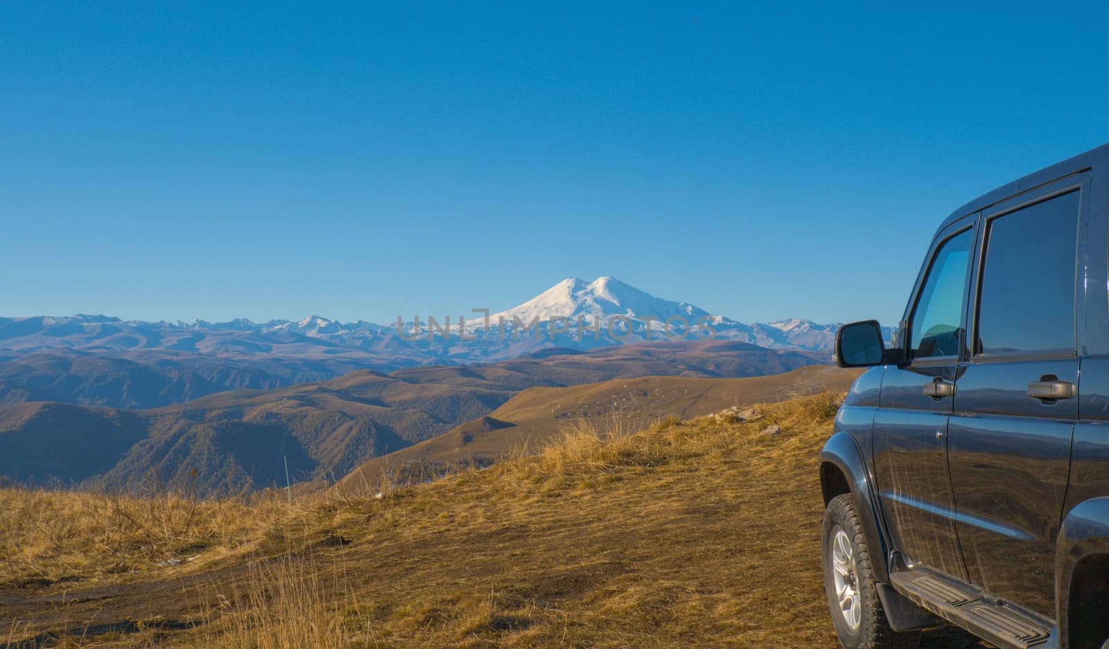 A car against the backdrop of a beautiful landscape, snow-capped Mount Elbrus and blue sky on autumn days by Ekaterina34