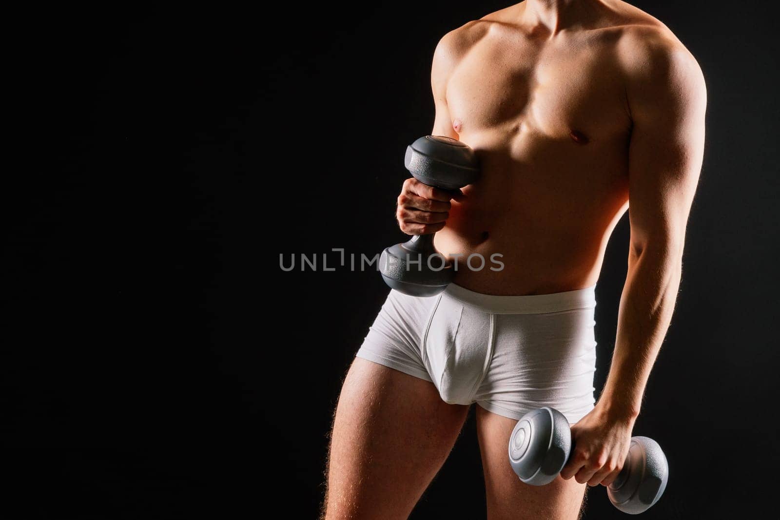 Studio shot of a muscular young man exercising with dumbbells against grey and black background.