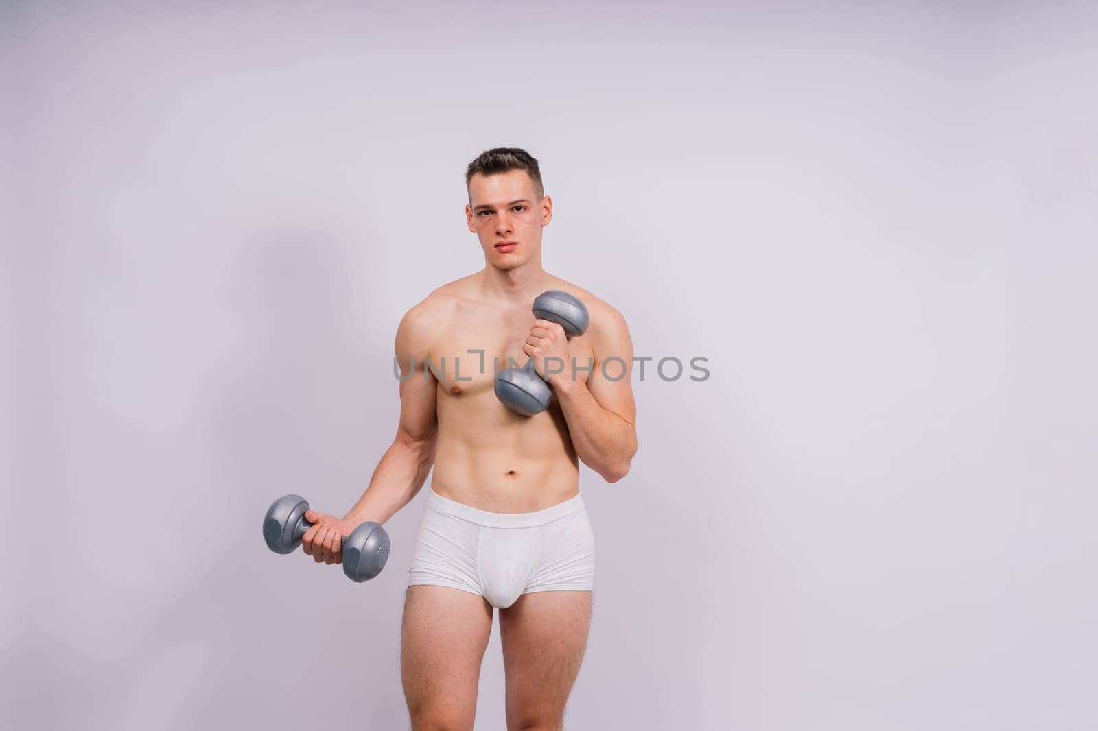 Studio shot of a muscular young man exercising with dumbbells against grey and black background.