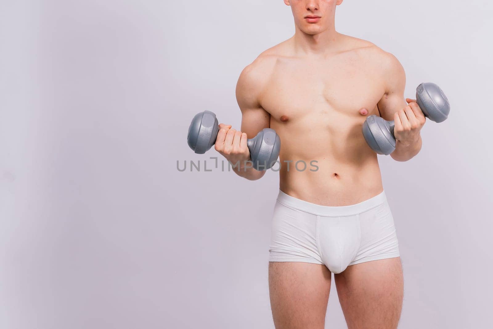 Studio shot of a muscular young man exercising with dumbbells against grey and black background.