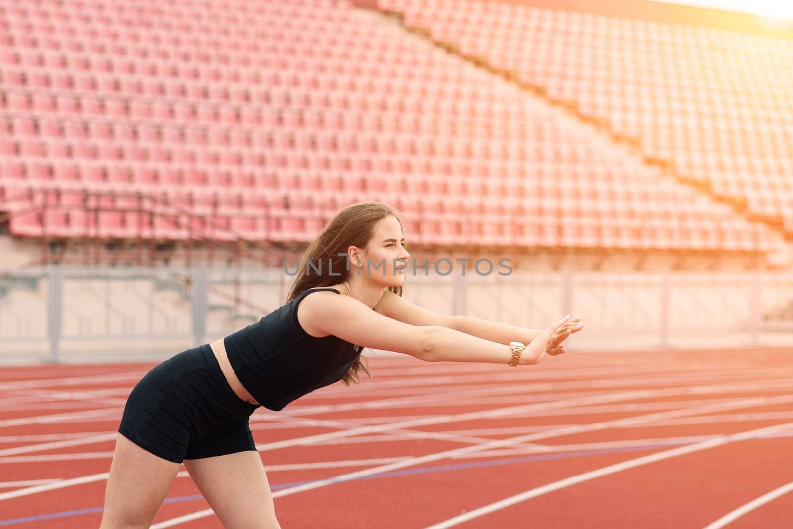 Young, beautiful girl athlete in sportswear is training and running, stretching at the stadium