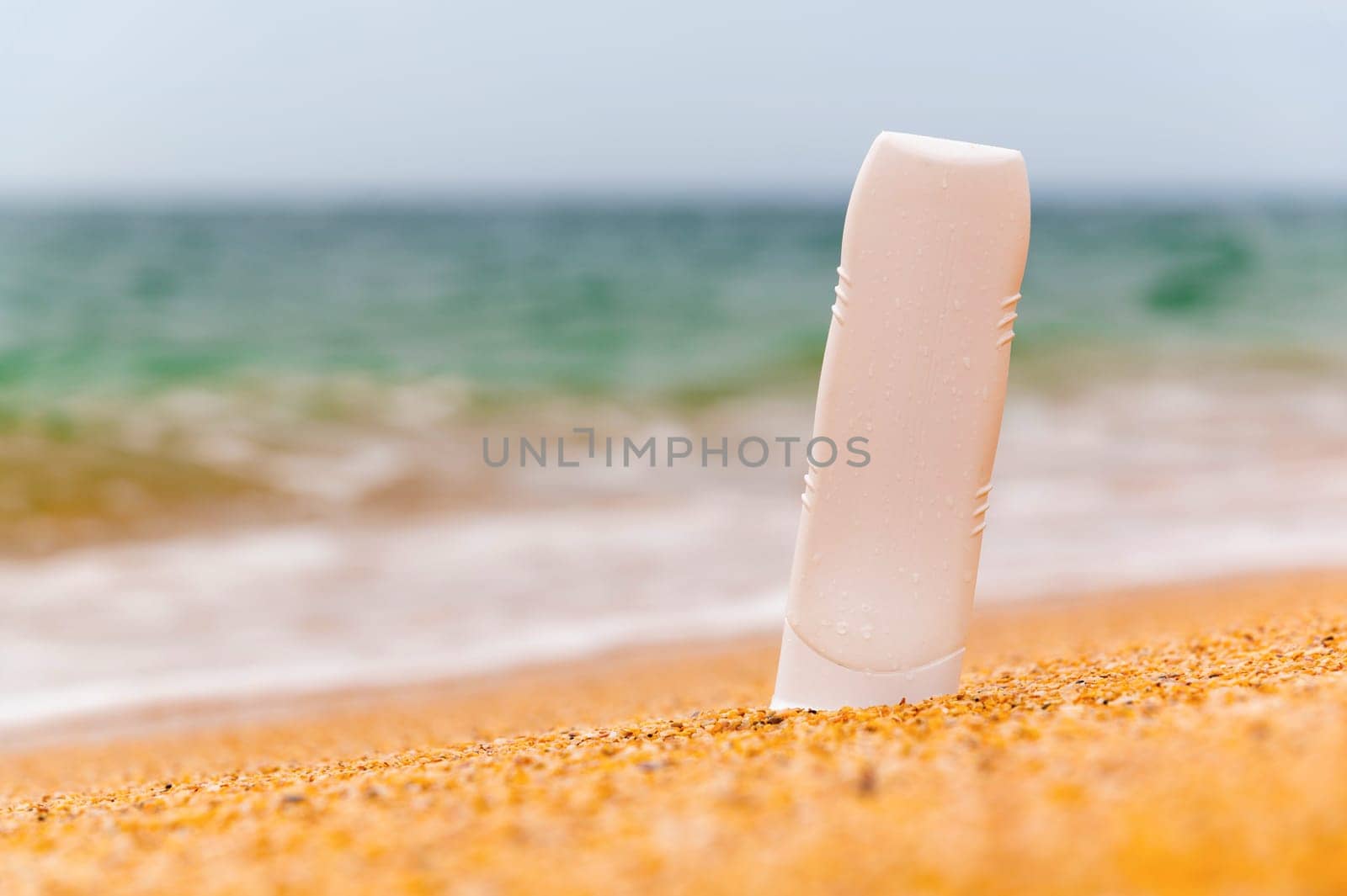 Bottle with sunscreen lotion on the beach, background of sea sky and waves, close-up. Layout for advertising a beauty product.