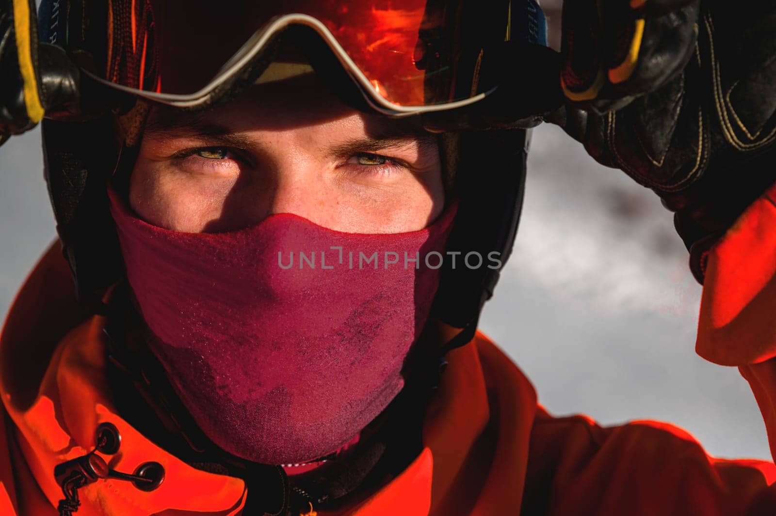 guy in ski goggles adjusts them on his face and wearing a protective helmet, close-up. A male skier has the sun shining on his face and stands against the backdrop of high mountains. Winter sport by yanik88