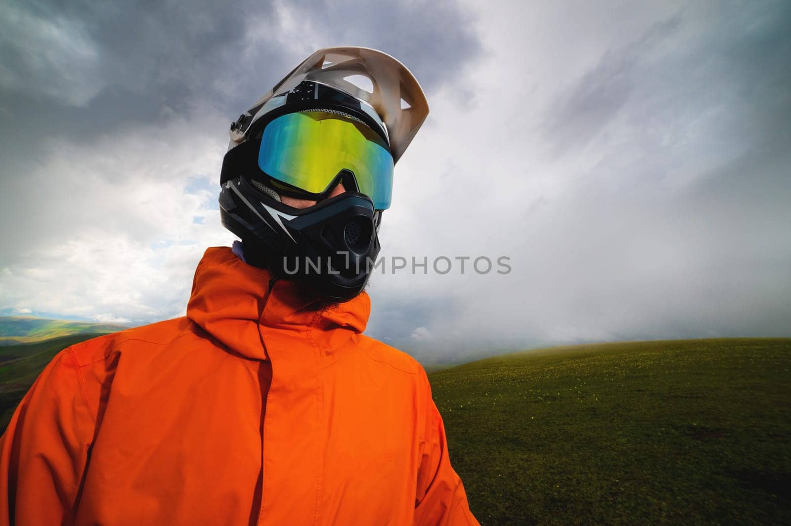 rider in a helmet and goggles, full protective equipment on an MTB bicycle or motorcycle stands on a rock against the backdrop of hills and low clouds by yanik88