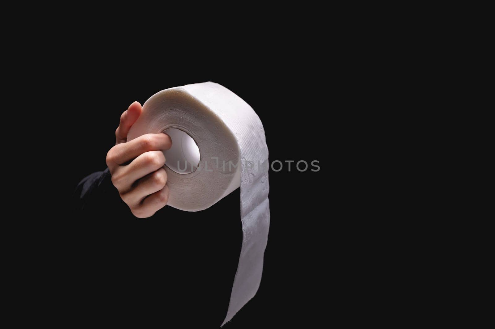 Close-up of a woman's hand holding out toilet paper, on a black background. A hand holds a roll of soft blank paper. White roll of toilet paper on a woman's hand.