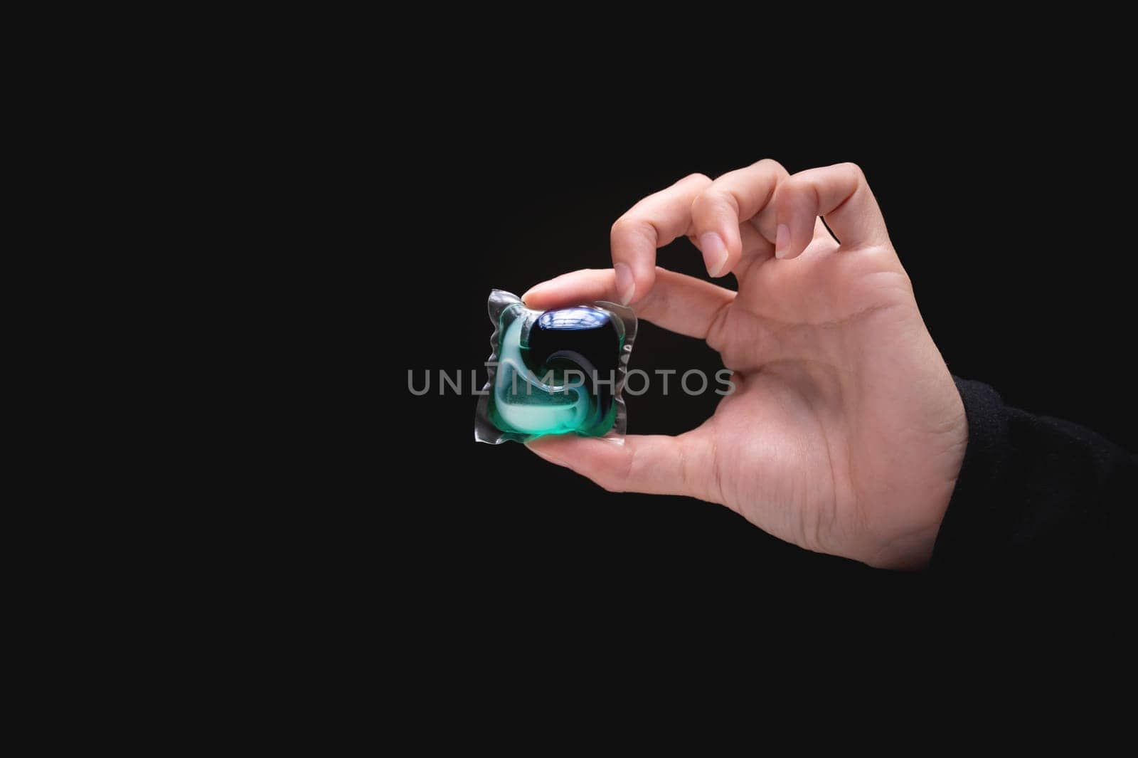 hand holds a capsule for a washing machine on a black background. female hand holding a tablet of detergent for washing clothes by yanik88
