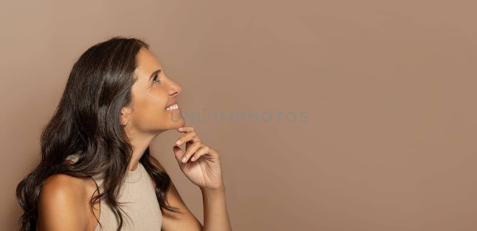 Pensive cheerful european old lady with natural makeup, enjoy skin care, look at free space, isolated on beige studio background. Beauty care, spa procedures, ad and offer