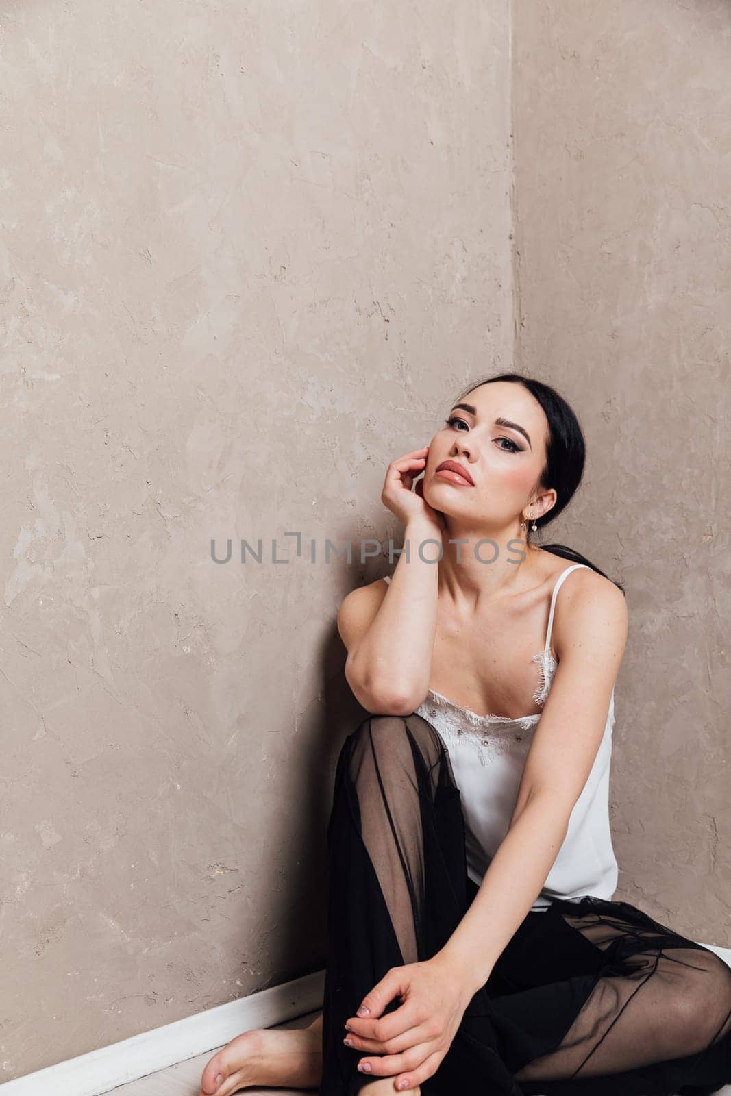 fashionable woman in black pants sits in a corner on the floor