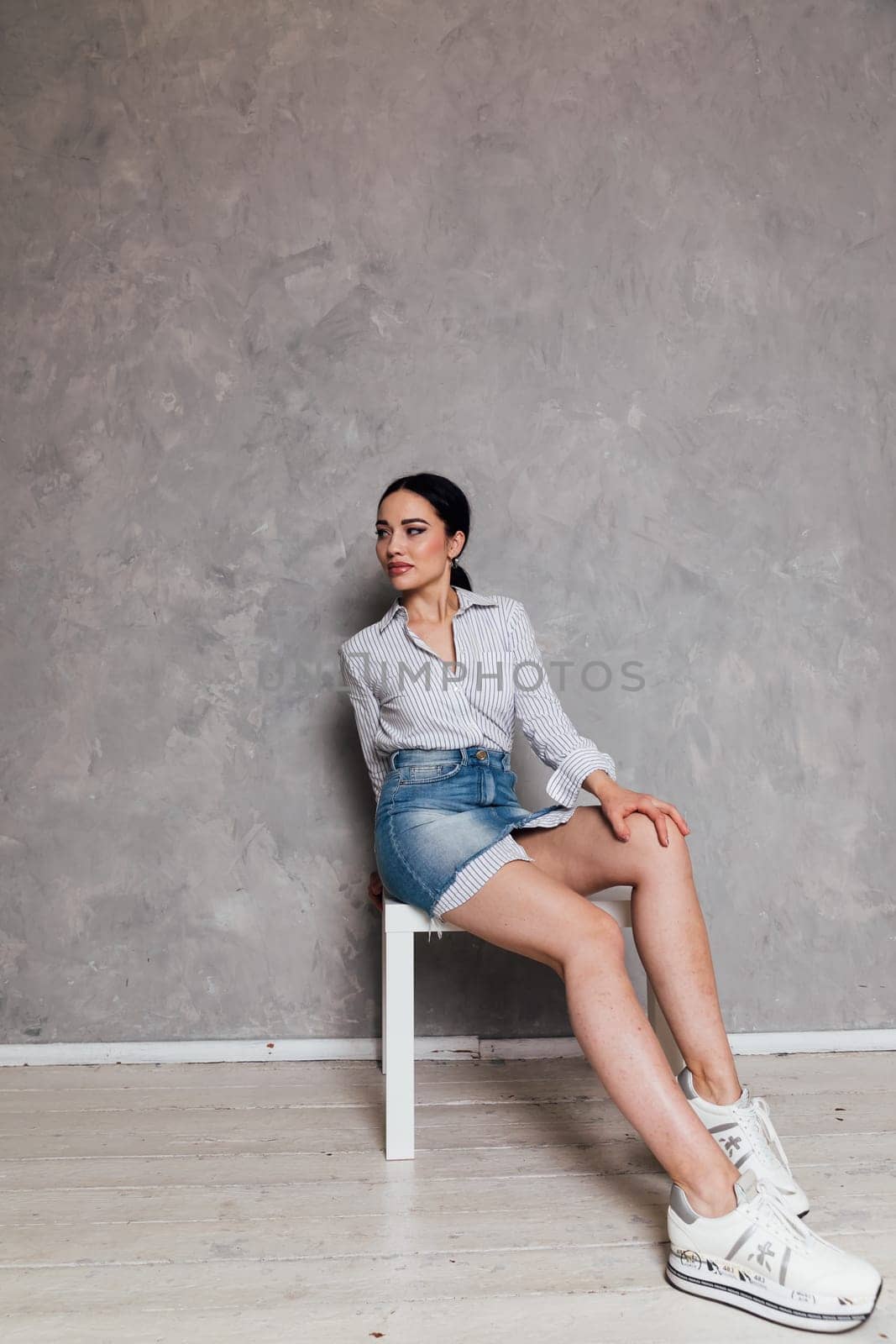 a woman in denim skirt sits on a chair in a room