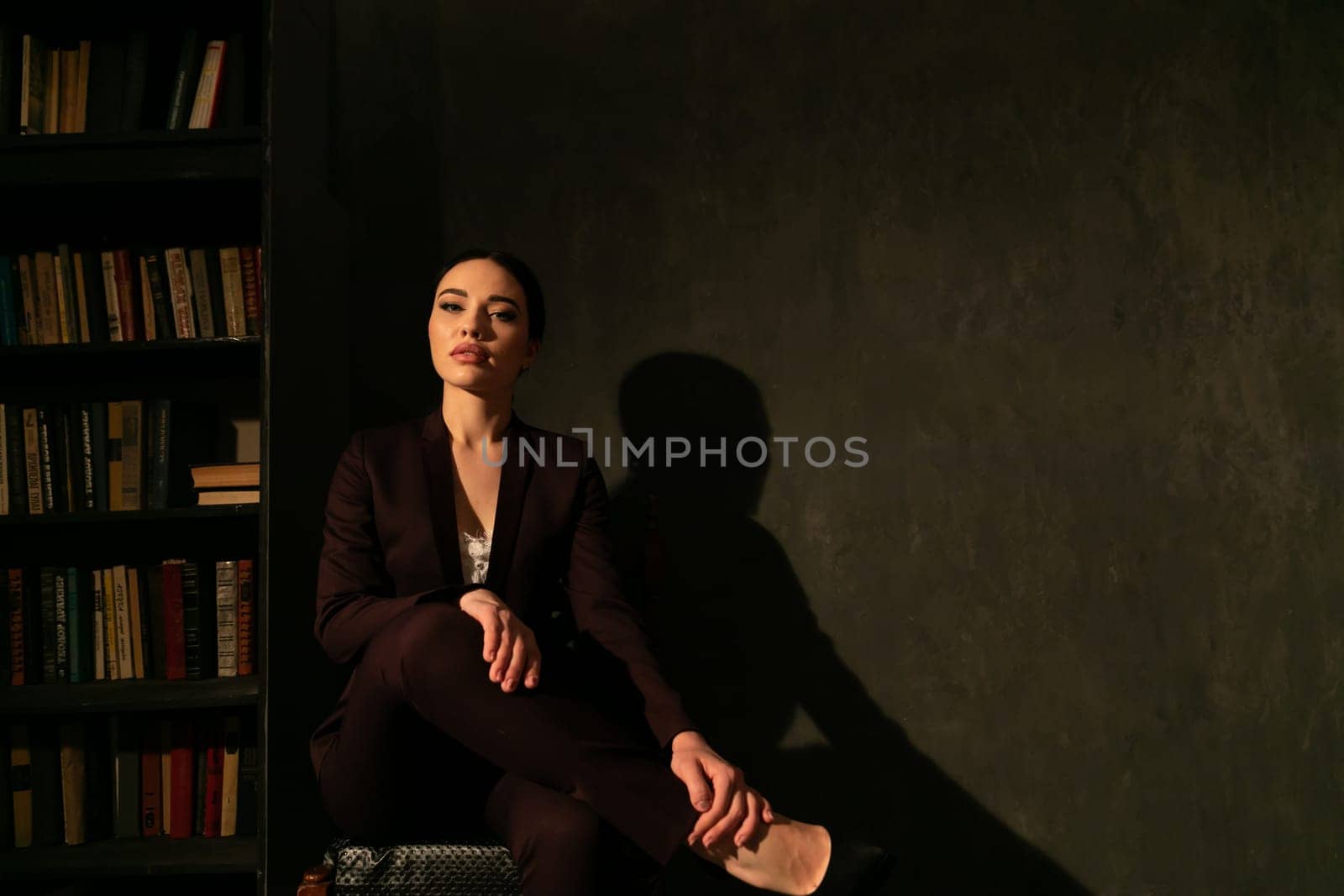 a woman sits in the shade in a room near books by Simakov