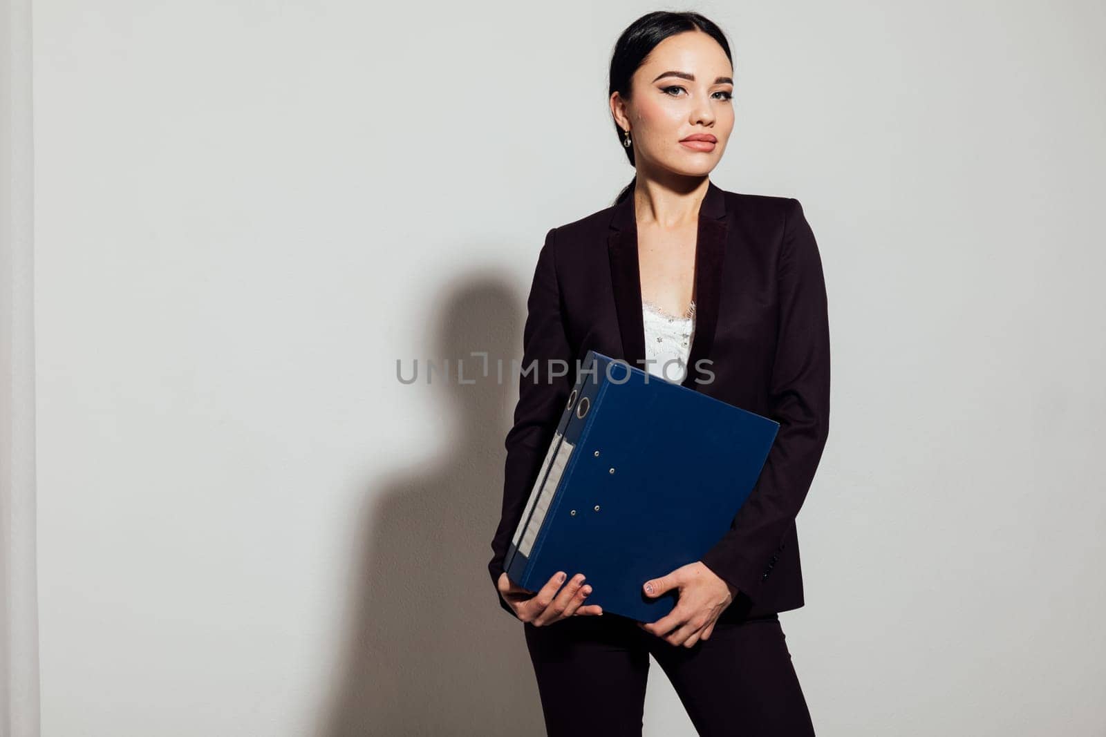 business woman in a black suit stands with a folder in an office space