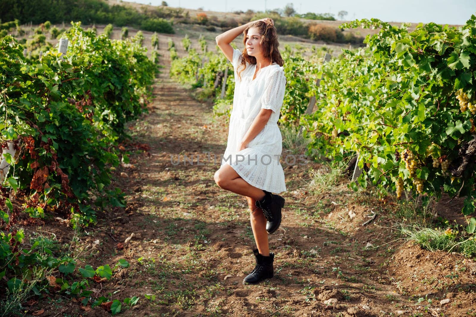 a woman in a white dress stands in the vineyards of country nature by Simakov