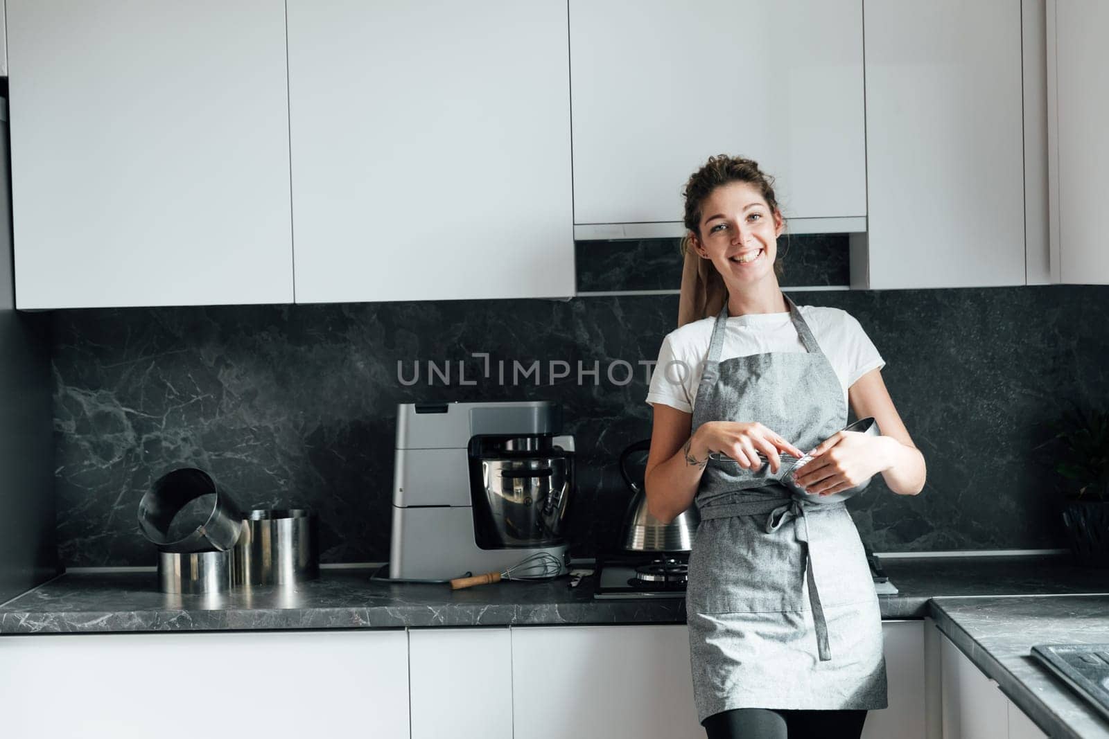 woman in an apron stands in the kitchen and cooks food in a bowl